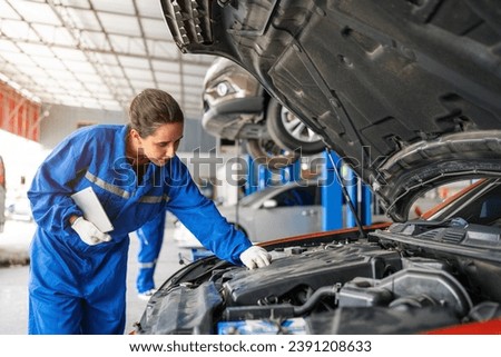 Mechanic working under the hood at the repair garage. Portrait of a happy mechanic woman working on a car in an auto repair shop. Female mechanic working on car. Female Auto Mechanic.