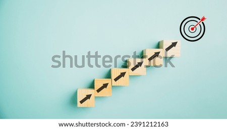 Target icon positioned on wooden blocks with upward arrows, depicting the progress. Blue background signifies business growth, while conveying concepts of profit, investment, and economic improvement. Royalty-Free Stock Photo #2391212163