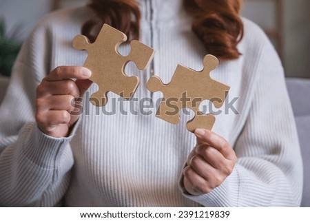 Closeup image of a woman holding and putting a piece of wooden jigsaw puzzle together