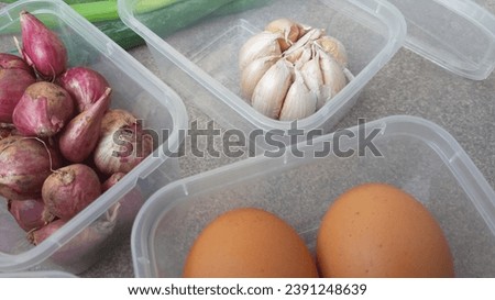 Shallots, eggs, and a bulb of garlic stored in open clear containers, with green onions placed outside—a dynamic visual of culinary preparation.