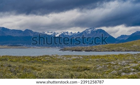 Picturesque snow-capped Andes mountains against a cloudy sky. In the foreground is the Beagle Channel, an island with sparse stunted vegetation of Patagonia. Argentina. Tierra del Fuego Archipelago.