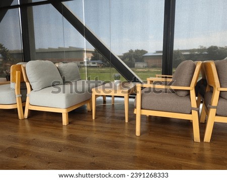 A living room on the second floor of a building.  The black steel frame is clear glass allowing for a view outside. There is a living room set, a table and wooden chairs with cream and gray cushions