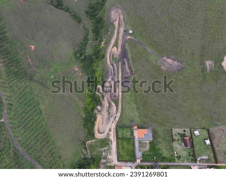 Top view of a rural motocross track with challenging turns and jumps, next to agricultural fields and facilities.