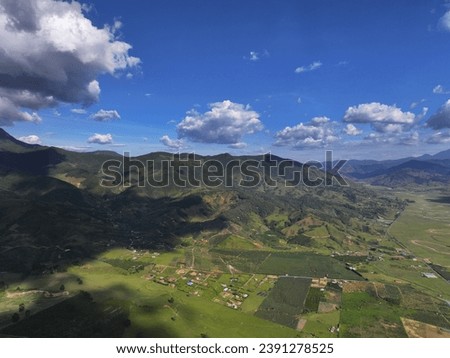 Breathtaking aerial perspective of a lush valley with agricultural patches and rural settlements, surrounded by hills under a partly cloudy sky.