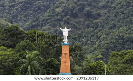 Statue of Jesus Christ with outstretched arms atop a pedestal, set against a dense mountain forest in Colombia.