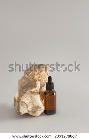 Amber Glass Cosmetic Bottle with Dropper with Serum or Cosmetic Skin Care Oil on Grey Background with Natural Stone. Vertical view