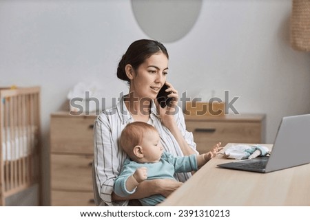 Portrait of young mother with baby working from home and talking on smartphone, copy space Royalty-Free Stock Photo #2391310213