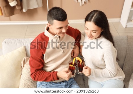 Happy couple with glasses of warm mulled wine sitting on sofa in living room