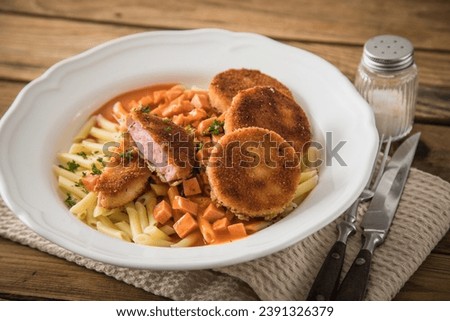 Jägerschnitzel escalope chasseur a East German DDR GDR specialty of breaded fried sausage slice, tomato sauce, Macaroni Penne pasta, parsley with porcelain plate, cutlery dark rustic wooden background Royalty-Free Stock Photo #2391326379