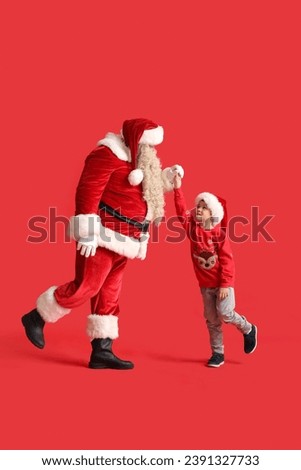 Santa Claus and cute little boy dancing on red background