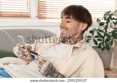 Tattooed young man with credit card using mobile phone at home
