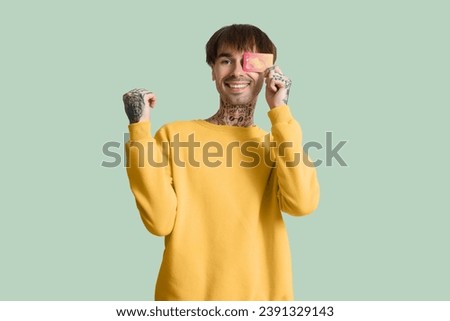 Tattooed young man with credit card on green background