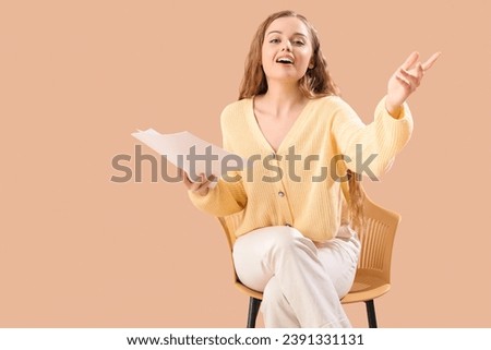 Beautiful actress with film script in chair on beige background Royalty-Free Stock Photo #2391331131