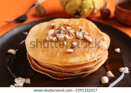 Plate of tasty pumpkin pancakes with honey and nuts on orange background, closeup