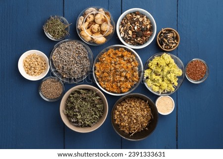 Many different dry herbs, flowers and seeds on blue wooden table, flat lay