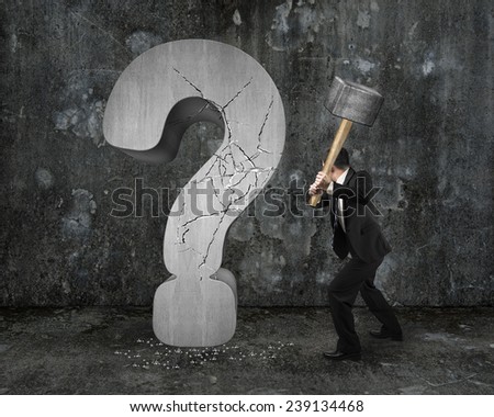 businessman holding hammer cracked question mark with gray mottled concrete wall background