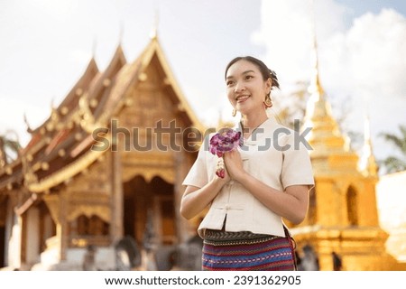 A beautiful Thai woman in a traditional Thai-Lanna dress with a garland is putting her hands together in a prayer position while standing in front of a beautiful chapel in a temple. make a wish Royalty-Free Stock Photo #2391362905