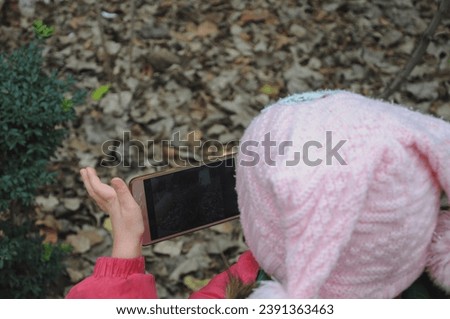 A girl with a phone walks in the park. The child takes photos on the phone.