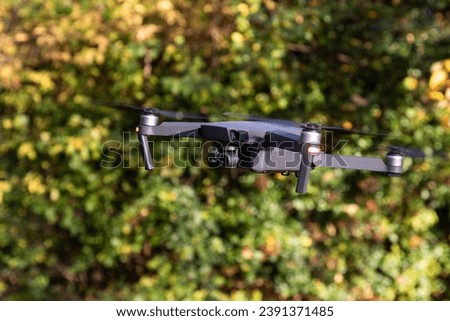 Drone with digital camera and fast rotating propellers flying taking video and pictures. Greenery backgroud
