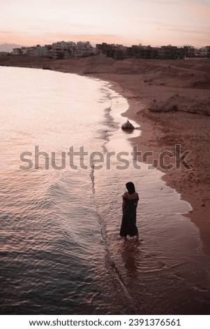 one girl in a dress walks along the seashore against the backdrop of a beautiful sunset. vertical image.