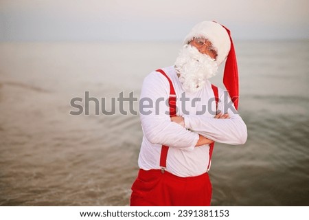 Santa in red suspenders with folded arms against the background of the sea. Christmas holidays at the sea.