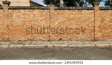 Old brick surrounding wall with a  worn concrete sidewalk and  urban street in front. Grunge background for copy space.