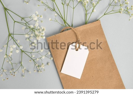 A mock-up of a white tag, label and price tag near a craft bag with flowers lie on a gray table. Empty space for text. Close-up