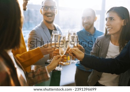 Colleagues in the office celebrate the concluded deal with champagne and sparkling wine. A group of people with glasses of champagne having fun, relaxing in the office. Concept of work, holiday. Royalty-Free Stock Photo #2391396699