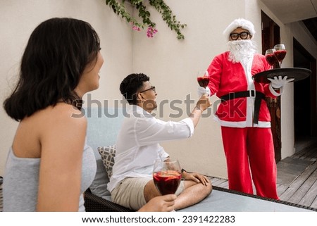 Santa serving drinks to a couple celebrating Christmas or New Year sitting and relaxing by swimming pool during tropical vacation