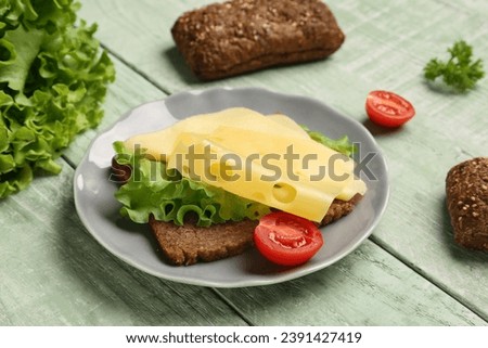 Tasty sandwich with cheese, lettuce and tomato in plate on green wooden background, closeup Royalty-Free Stock Photo #2391427419