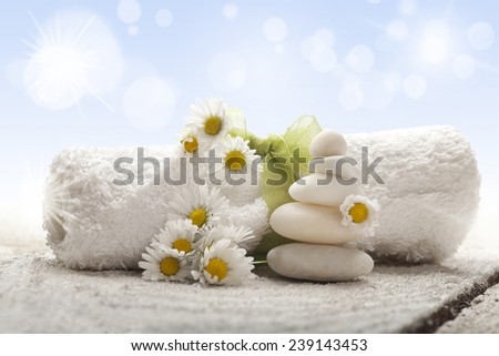Spa background with rolled towel, chamomile and white stones on old wooden background. 