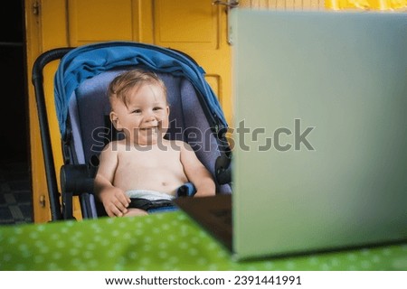Happy baby boy sitting and watching cartoons on modern wireless computer laptop. The child smiles in a cheerful mood