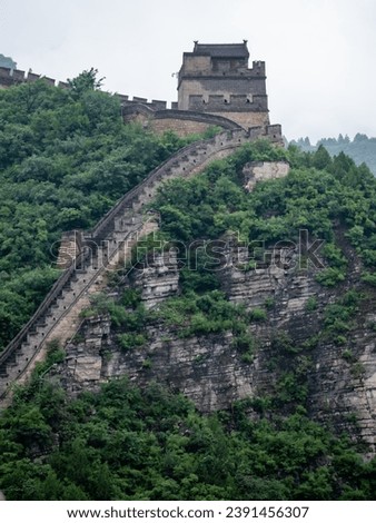 The Great Wall of China winds its way through the mountains, its towers and ramparts rising up from a lush green landscape. The photo is a stunning depiction of the beauty and history of this ...