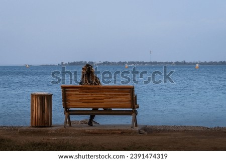 Young woman looking back sitting on a bench by the sea