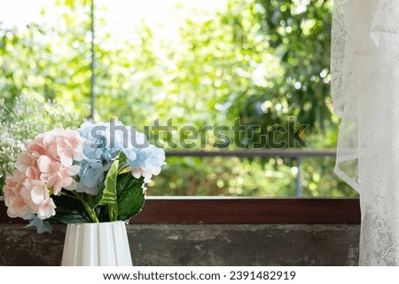 Beautiful and cozy style background with copy space of colorful flowers in vase with wooden frame of window in vintage or retro decoration seeing natural summer sunlight on greenery trees and leafs.