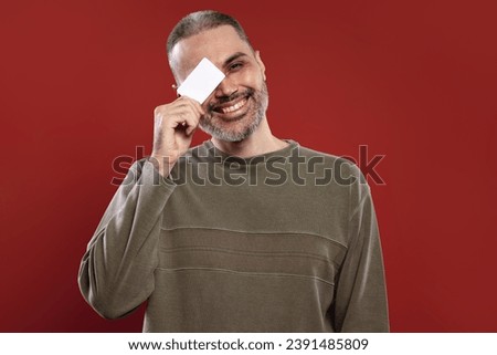 Smiling man holding a white card and covering one of his eyes