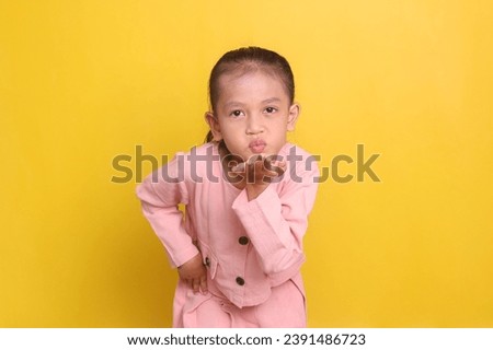 Adorable Asian little girl blowing a kiss isolated on yellow background