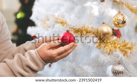 Senior people stay at home alone on Christmas holidays concept. Close up elder woman hand decor xmas tree at living room.