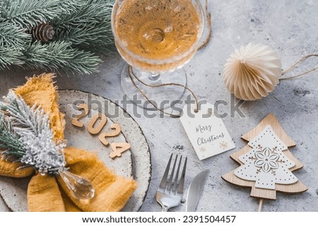 Table setting. Stylish plates, napkin, glass, champagne, Christmas tree branches and Christmas decorations on a gray background. The concept of merry Christmas and New Year 2024.