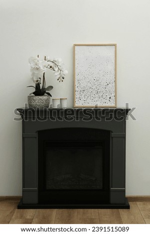 Picture frame, candles and orchid on fireplace near white wall indoors. Interior design