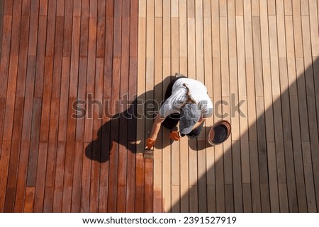 Workwoman staining wood deck boards outdoors, full body overhead view. Space for text Royalty-Free Stock Photo #2391527919
