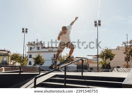 Low angle back view of male athlete in sportswear performing trick on skateboard while training in skate park with tree on sunny day