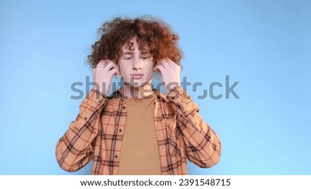 A young man listens to music in wireless headphones isolated on a blue studio background