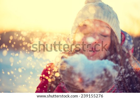 Beauty Winter Girl Blowing Snow in frosty winter Park. Outdoors. Flying Snowflakes. Sunny day. Backlit. Joyful Beauty young woman Having Fun in Winter Park. Defocused Royalty-Free Stock Photo #239155276