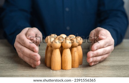 A man protects human figures with his hands. The concept of security and social protection. Health coverage benefits, retirement plans. Creating an environment where everyone feels secure and valued. Royalty-Free Stock Photo #2391556365
