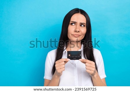 Photo of suspicious unsure lady wear white shirt holding credit card looking empty space isolated blue color background