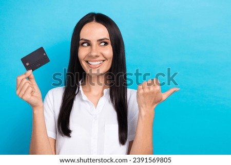 Photo of dreamy cute lady wear white shirt holding credit card looking pointing thumb empty space isolated blue color background