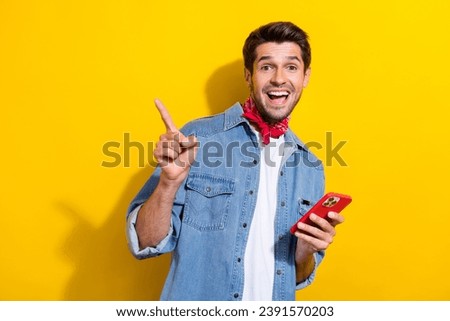 Photo portrait of attractive young man point empty space hold device wear trendy jeans clothes isolated on yellow color background