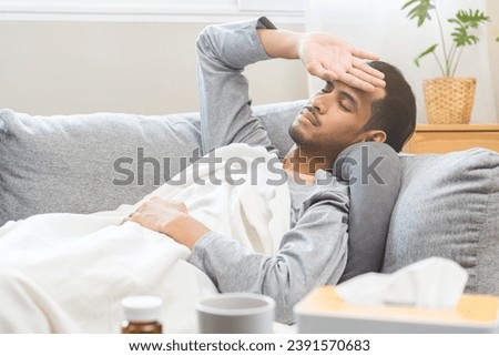 Sick, influenza asian young man, male have fever hand touching forehead for check measure body temperature, illness while lying rest on sofa at home. Health care on virus person. Royalty-Free Stock Photo #2391570683