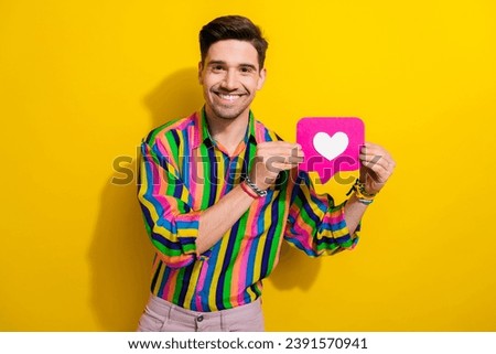 Portrait of young macho blogger hold heart button click like for his new video about picking up girls isolated on yellow color background